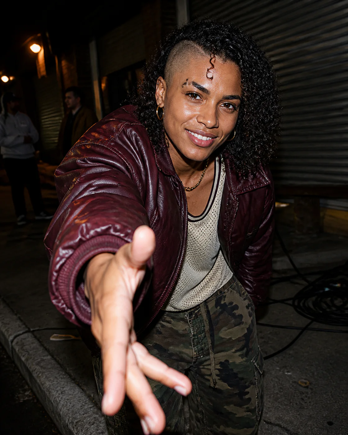 Roxy Valdez in an oxblood bomber outside a Brooklyn rehearsal warehouse, reaching forward to offer a dap.