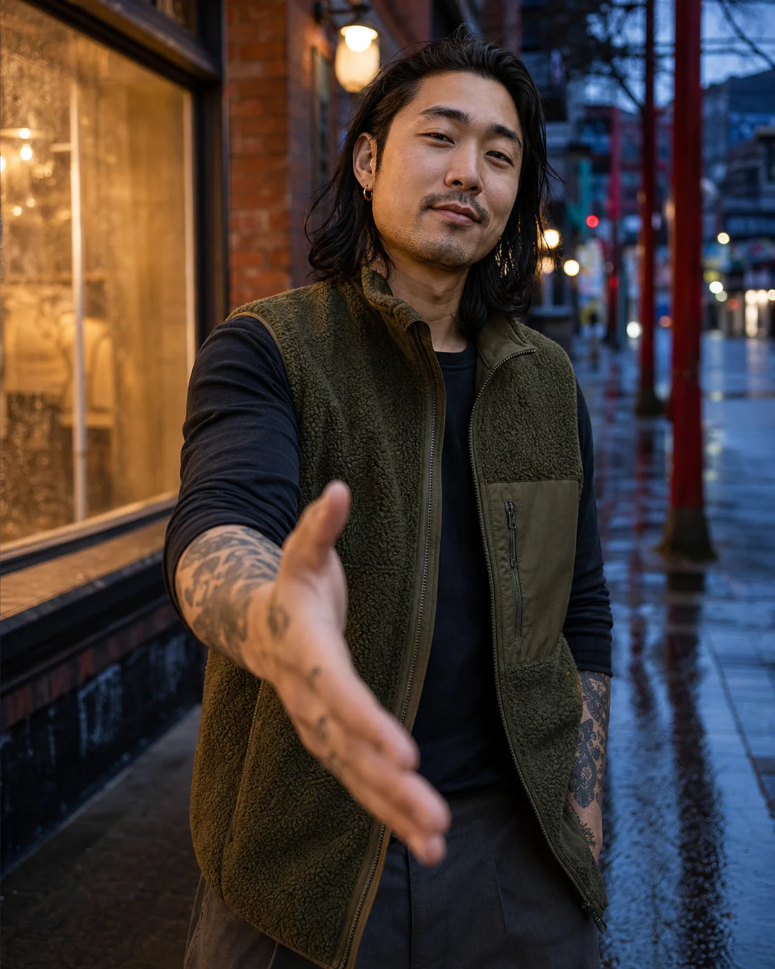 Vince Park in an olive fleece vest on a rain-slick Vancouver street, reaching forward to offer a dap.